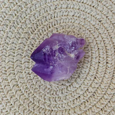 An amethyst crystal rests on a woven surface